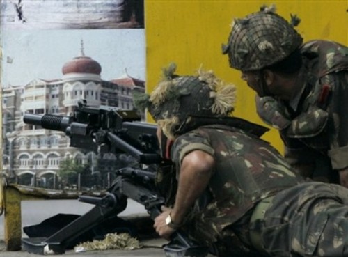 Army personnel lie down near a tourism poster and aim a grenade launcher at a part of the facade of the Taj Mahal hotel, unseen,  in Mumbai, India, Friday, Nov. 28, 2008. Explosions and gunfire continued intermittently at the Taj Mahal hotel Friday afternoon,two days after a chain of militant attacks across India's financial center left people dead and the city in panic. (AP Photo/Rajanish Kakade)